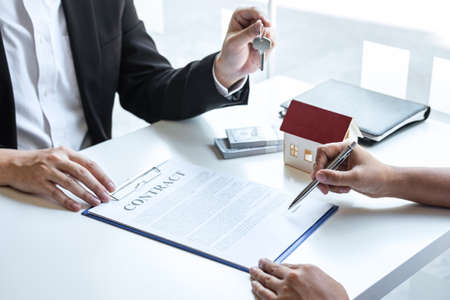Estate agent giving house keys to client after signing agreement contract real estate with approved mortgage application form, concerning mortgage loan offer for and house insurance.の写真素材