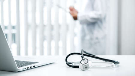 Doctor is standing and reading report and Stethoscope is on the table, doctor is reading symptoms of the patient and analyze treatment, health care and medicine at his hospital officeの写真素材