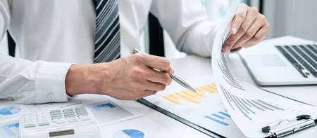 Business man hold pen to check investment data with a calculator, the chart contains costs expenses profits use in the businessの写真素材