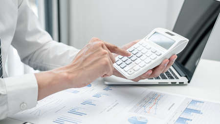 Business man press calculator to check investment data, by examining data from various chart in the bookの写真素材