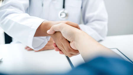 The doctor shakes hands with his patients at his hospital office, doctor talk closeup with patient about good results and to advice health care and medicineの写真素材