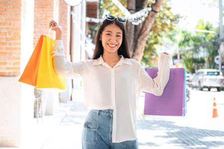 Asian woman shopaholic smiling with many colorful shopping bags and holding credit card for payment...