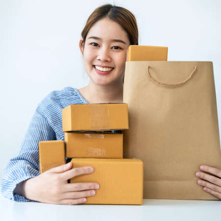 Asian woman small business owner smiling with many parcel of box to preparing order delivery to customer at home while sitting to working in home officeの写真素材