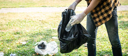 Volunteer man in gloves to picking up plastic bottle into plastic black bag for cleaning the park during environmental activity to collecting garbageの写真素材