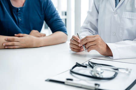 Doctor and patient are discussing symptoms at hospital office, doctor are giving advice on the effects of symptoms and treatment, medicine, and healthcare to the patientの写真素材