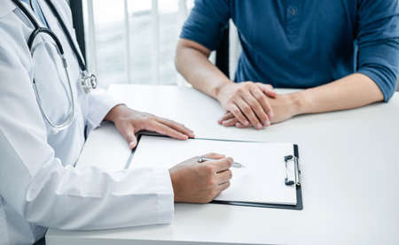 Doctor is explaining the symptoms to the patient at medical clinic, doctor is reading the details of the treatment health care and writing prescriptions to the patientの写真素材