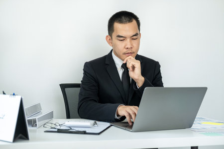 Businessman boss in suit is thinking and analysis of investments in new business from chart during to typing new idea for business project and financial data while sitting to working in officeの写真素材