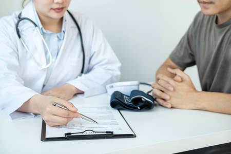Doctor is pointing on document to explaining disease and illness symptoms for patient before writing a prescription and giving treatment advice to patient in her clinicの写真素材