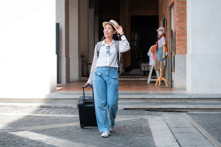 Asian woman tourist is traveling on holiday trip with hat and dragging her black luggage while walking to passengers lounge in the airportの写真素材