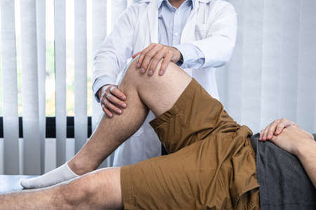 Young asian physiotherapist checking knee joint with injury to giving treatment and to rehabilitation therapies in clinicの写真素材