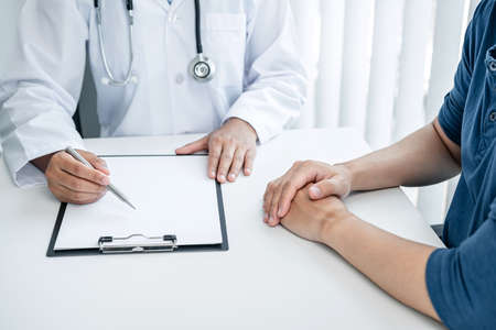 Doctor is explaining the symptoms to the patient at medical clinic, doctor is reading the details of the treatment health care and writing prescriptions to the patientの写真素材