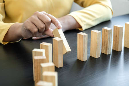 Risk and Strategy in Business, Image of hand stopping falling collapse wooden block dominoes effect from continuous toppled block, prevention and development to stability.の写真素材