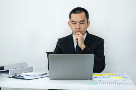 Businessman boss in suit is thinking and analysis of investments in new business from chart during to typing new idea for business project and financial data while sitting to working in officeの写真素材