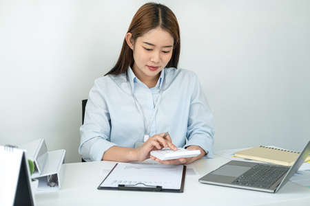 Woman office worker sitting to working and pressing a calculator to calculate the profit of a new business project and having happiness when job well doneの写真素材