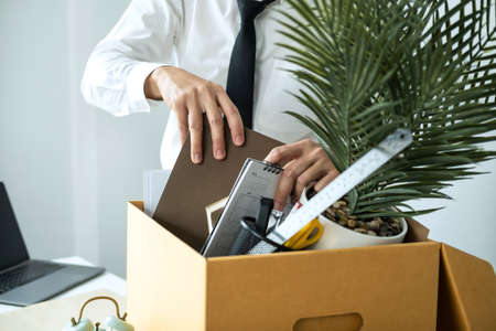 Business man employee packing notebook and picking up personal belongings into brown cardboard box to leaving workplace when resignation from work or changing workの写真素材