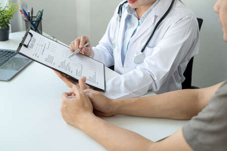 Doctor is pointing on document to explaining disease and symptoms for patient during to talking about diagnostic, medicine and to giving advice to patient in her clinicの写真素材