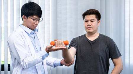 Young asian physiotherapist gives advice on how to properly lifting dumbbells during physical therapy sessions in the clinicの写真素材