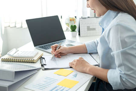 Woman office worker sitting to working and writing business project report on clipboard during checking information on document and smiling when job finishedの写真素材