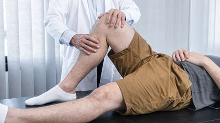 Young asian physiotherapist checking knee joint with injury to giving treatment and to rehabilitation therapies in clinicの写真素材
