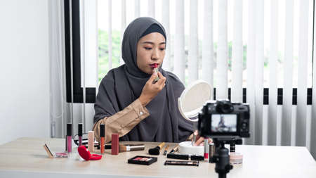 Asian muslim woman beauty blogger tutorial by lipstick makeup on her mouth and making videos to review cosmetic products for her vlog and blogger to share on website or social mediaの写真素材