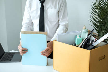 Business man employee packing document and picking up personal belongings into brown cardboard box to leaving workplace when resignation from work or changing workの写真素材