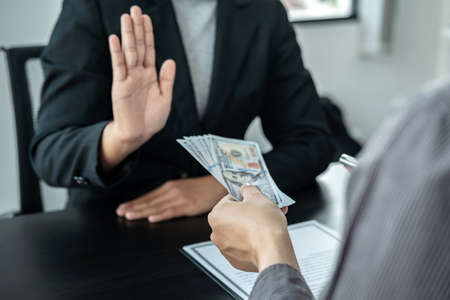 Close up of man employee offering bribe money to businessman to signing the contract to joint engage in illegal and immoral project while he refusing an offerの写真素材