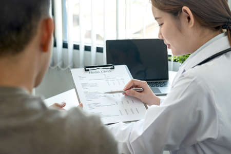 Doctor is pointing on document to explaining disease and symptoms for patient during to talking about diagnostic, medicine and to giving advice to patient in her clinicの写真素材