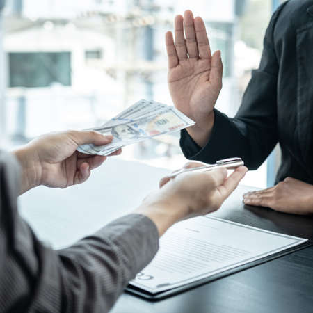 Close up of man employee offering bribe money and pen to businessman to signing the contract to joint engage in illegal and immoral project while he refusing an offerの写真素材