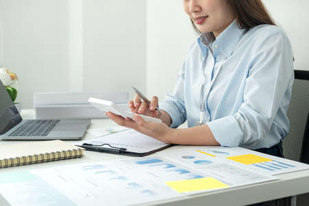 Woman office worker sitting to working and pressing a calculator to calculate the profit of a new business project and having happiness when job well doneの写真素材