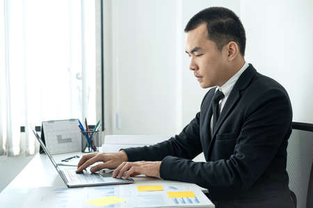 Businessman boss in suit to analysis of investments in new business from chart and document during to typing new idea for business project and financial data while sitting to working in officeの写真素材
