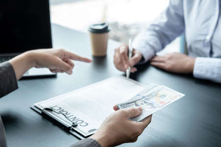 Man employee giving bribe money to business woman and pointing at the contract signing box while she is holding pen signing to joint engage in illegal and immoral projectの写真素材