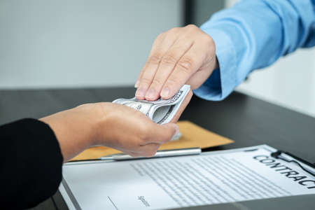 Close up of man employee receiving bribe dollars in his hands from businessman after signing the contract to engage in illegal and immoral project of corruptionの写真素材