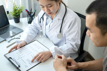 Doctor is pointing on document to explaining disease and illness symptoms for patient before writing a prescription and giving treatment advice to patient in her clinicの写真素材
