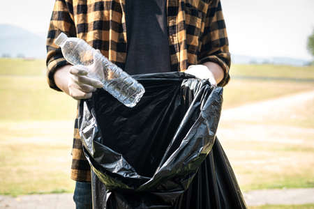 Close up of volunteer man in gloves to picking up plastic bottle into plastic black bag for cleaning the park during environmental activity to collecting garbageの写真素材