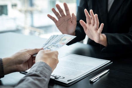 Close up of man employee offering bribe money to businessman to signing the contract to joint engage in illegal and immoral project while he refusing an offerの写真素材