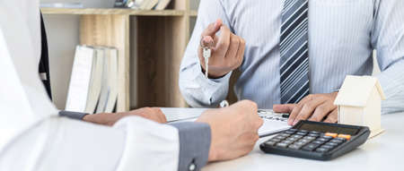 Estate agent giving house keys to client after signing agreement contract real estate with approved mortgage application form, concerning mortgage loan offer for and house insurance.の写真素材