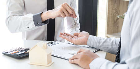 Estate agent giving house keys to client after signing agreement contract real estate with approved mortgage application form, concerning mortgage loan offer for and house insurance.の写真素材