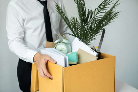 Business man employee stressful resignation from job while picking up personal belongings into brown cardboard box and carrying to walking out from officeの写真素材