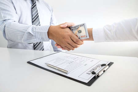 Dishonest cheating in business illegal money, Businessman handshake with money of dollar banknotes in hands from while give success the deal, Bribery and corruption concept.の写真素材