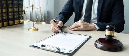 Counselor lawyer or notary working on a documents and report of the important case and wooden gavel, brass scale on table in courtroom.の写真素材