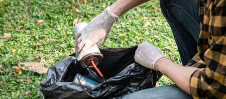Volunteer man in gloves sitting to picking up coffee cup into plastic black bag for cleaning the park during environmental activity to collecting garbageの写真素材