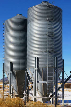Two grey silos at a farm during the winter.の写真素材