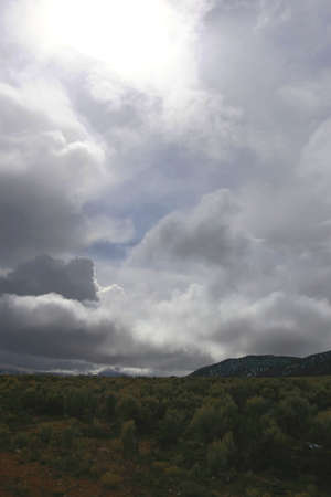 Dark landscape with towering white clouds and bright sky.の写真素材