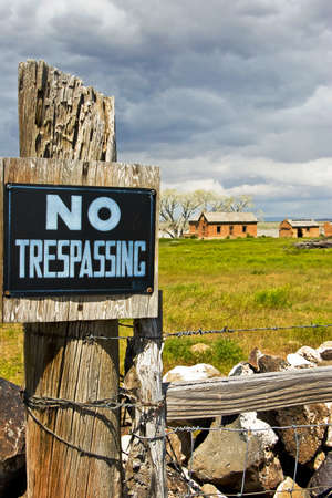 A NO TRESPASSING sign on a fence blocks access to an abandoned farm.の写真素材