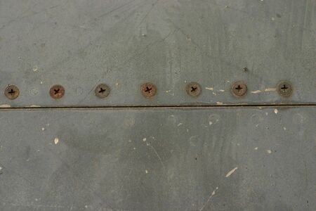 A line of rusty screws on an old metal plateの写真素材