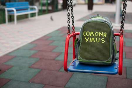 Empty playground with backpack with inscription coronavirus on a swing.の写真素材