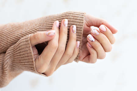 Pastel beige manicure on the light background. Manicured nails and soft hands skin with copy space. Womans hands in warm sweater.の写真素材