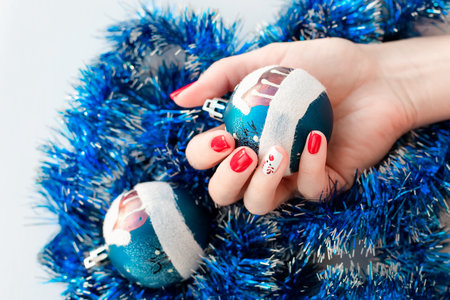 Red winter manicure with cute deer on festive background. Woman holding Christmas ball. Winter and Christmas time concept.の写真素材