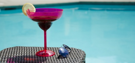 Coctail and sunglasses on summer wicker chair by the pool