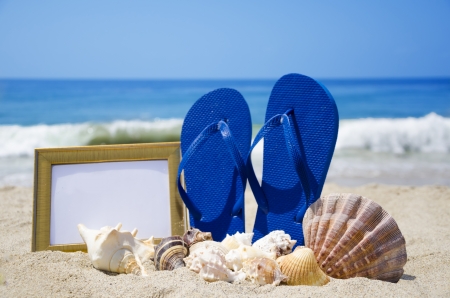 Flip-flops with photoframe and seashells on sandy beachの写真素材